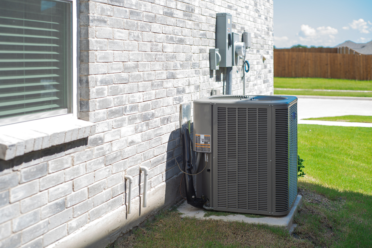 Side windows of new construction home and central air conditioning condenser unit mounted on concrete slab beside brick house wall, utility meters and electrical disconnect, suburbs Dallas, Texas